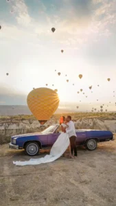 Couple hugging and standing near a car with hot air balloon background